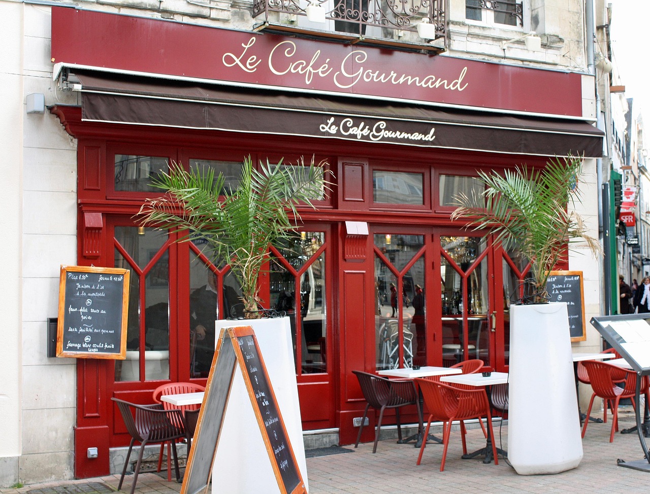Französisches Café mit roten Fensterläden und Außentischen.